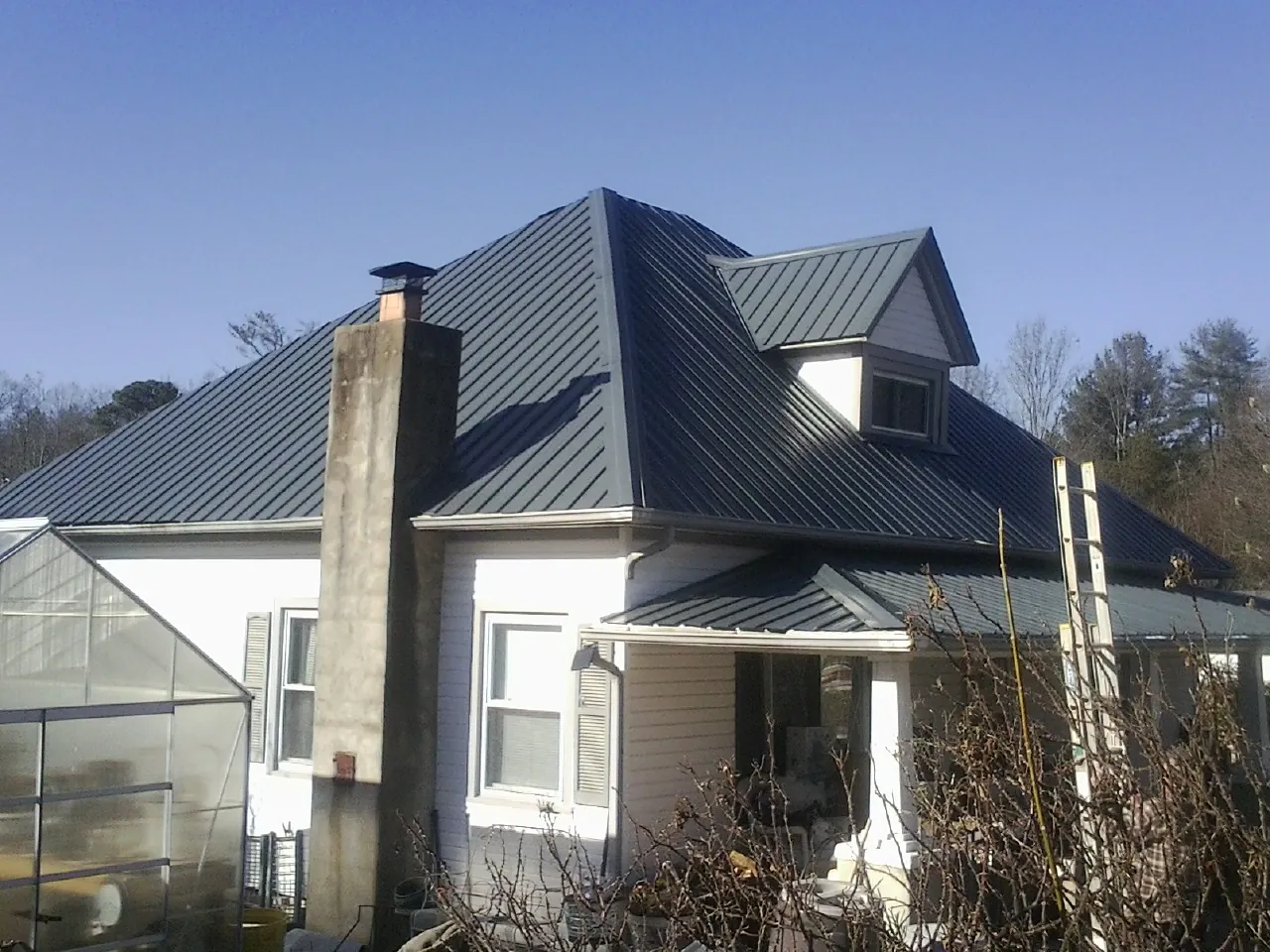Dark blue standing seam metal roof on a white farmhouse with dormer — Slate & Tile Roof Repair by Roofing Brothers in Brookpark