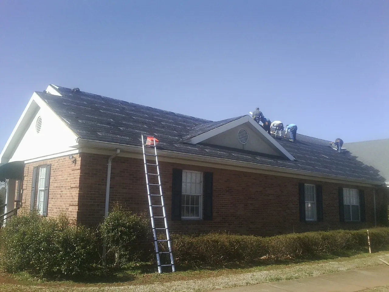 Crew tearing shingles off a brick ranch roof with a ladder set — Emergency Roof Repair work by our crew in Brookpark