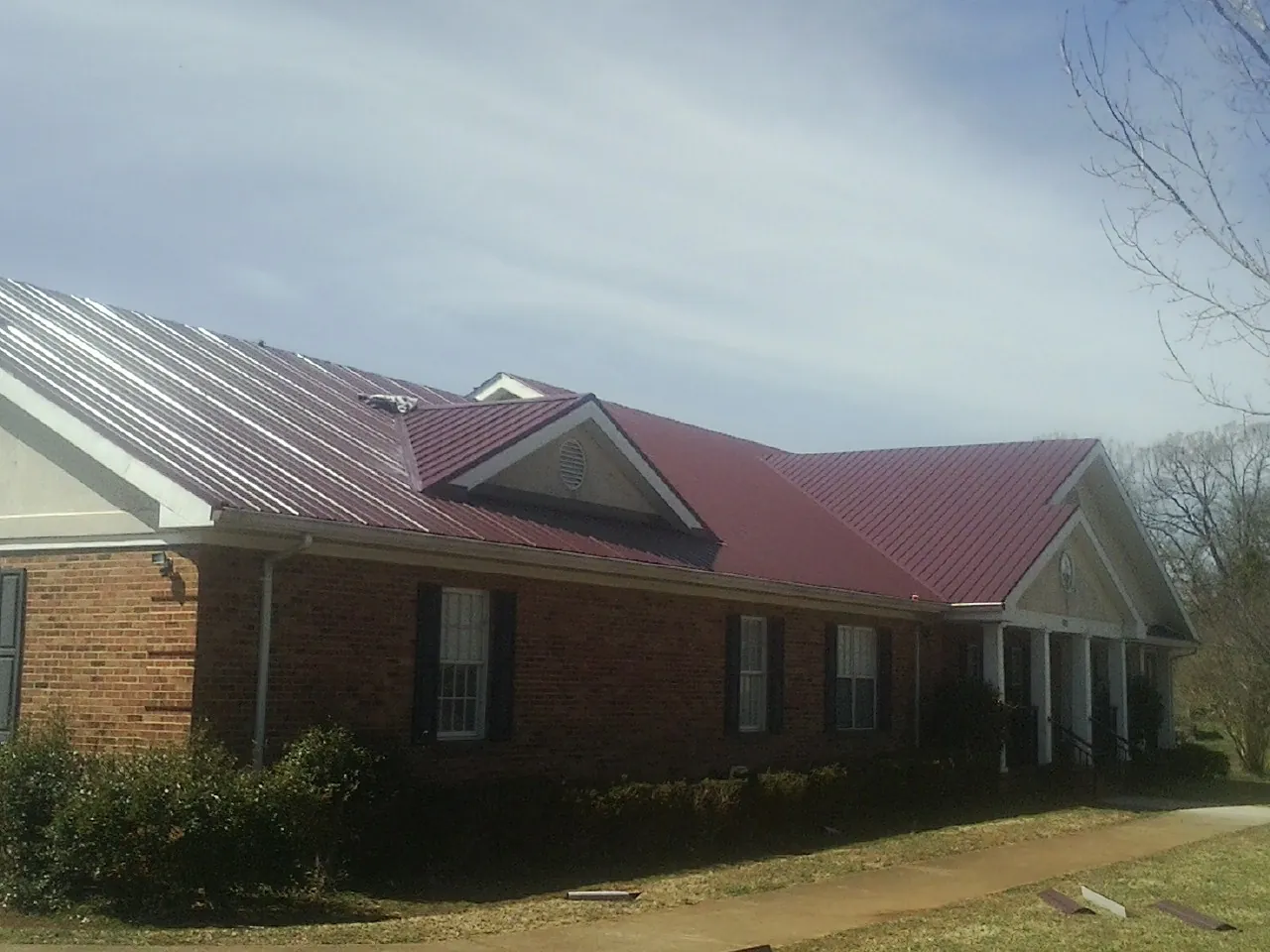 Red metal roof with gabled entries on a long brick building, from a Hail Damage Roof Repair job in Brookpark