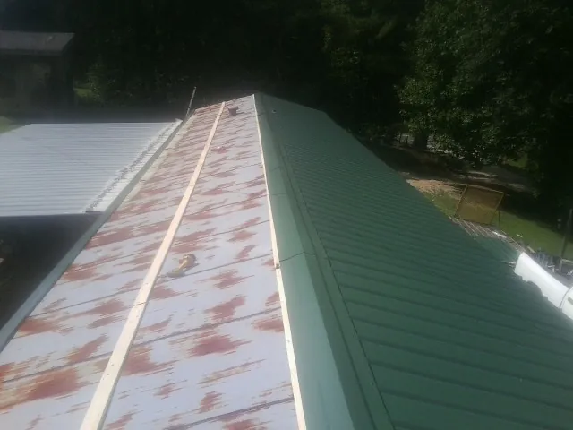 Old rusted panels beside newly installed green metal roofing — Wind Damage Roof Repair by Roofing Brothers in Brookpark