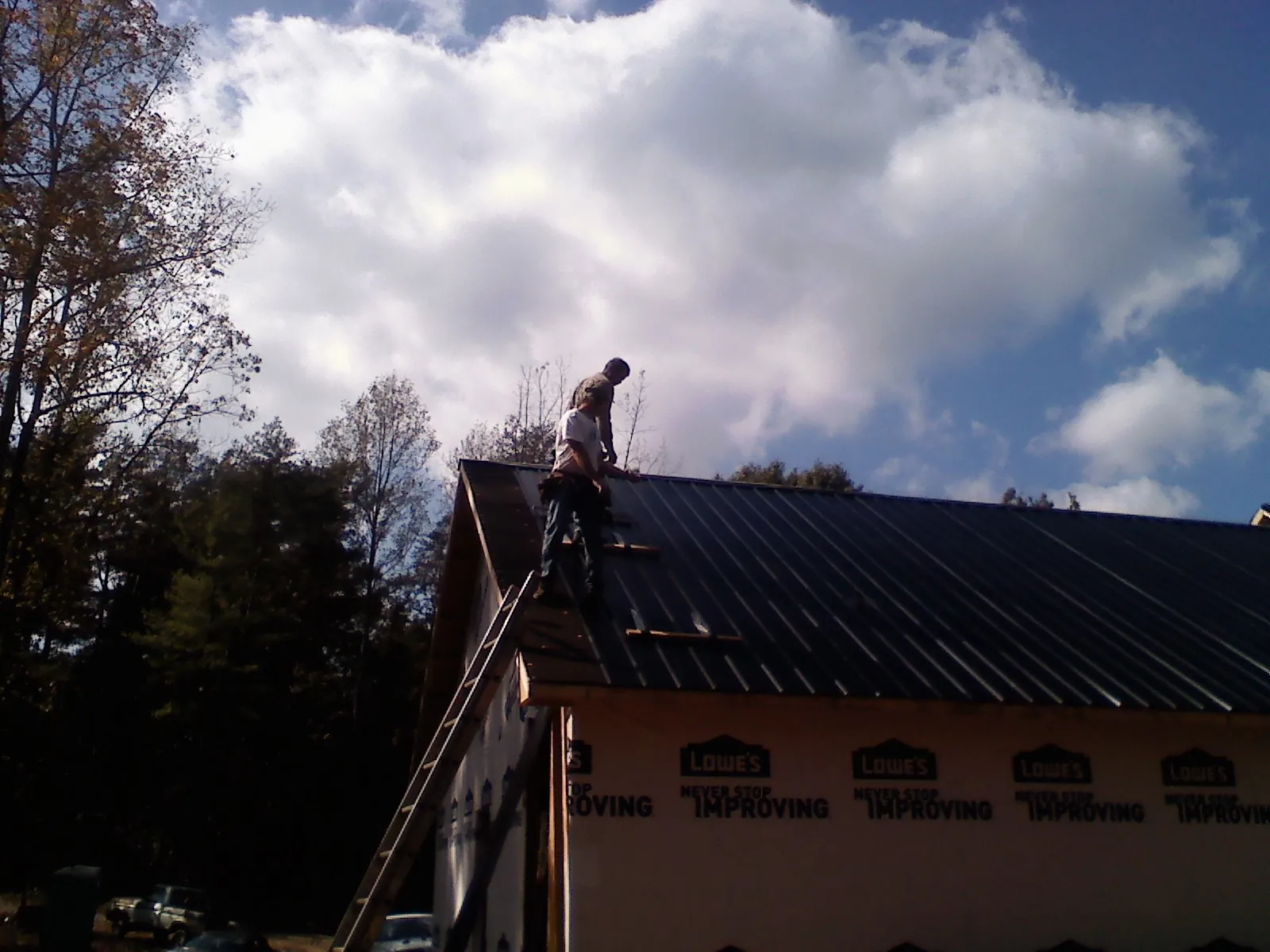 Roofer fastening dark metal panels high against a cloudy sky, from a Roof Inspection job in Brookpark